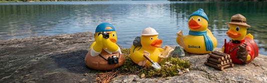 Quebec explorer rubber ducks with camera, backpack, and Mountie gear beside a lake